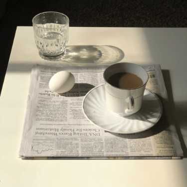 Coffee, water and an egg sitting on newspaper.