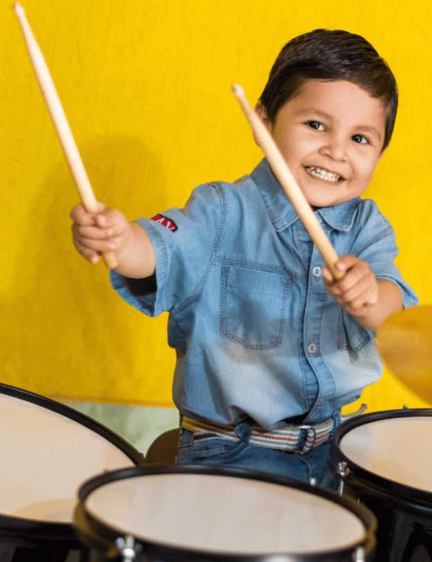 A colored child sitting behind a drum set posing.