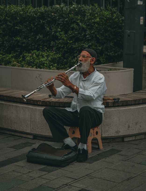 Old man playing a flute on the sidewalk.