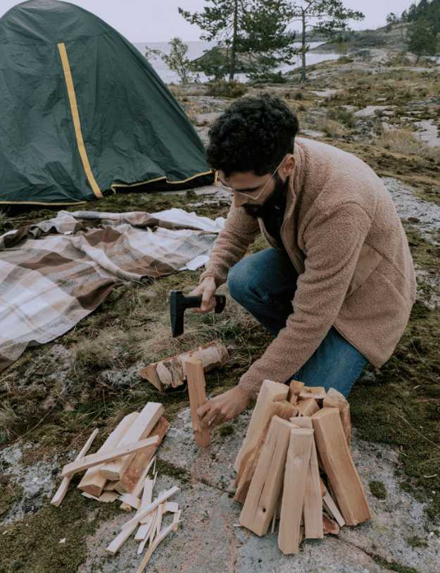 A man splitting wood with a hatchet next to a camp site.
