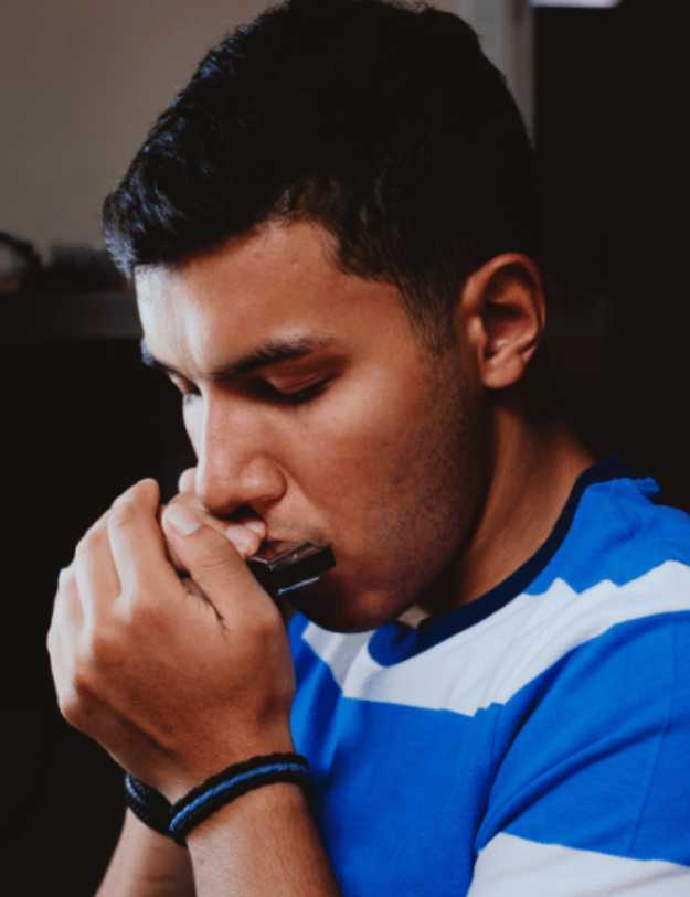  man in blue shirt playing a harmonica.