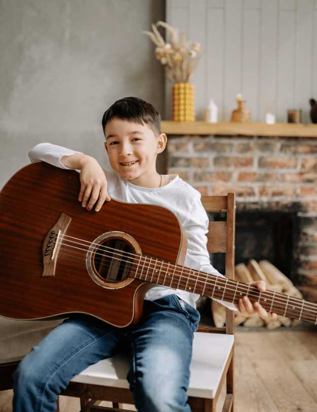 A child posing with a guitar while sitting down.