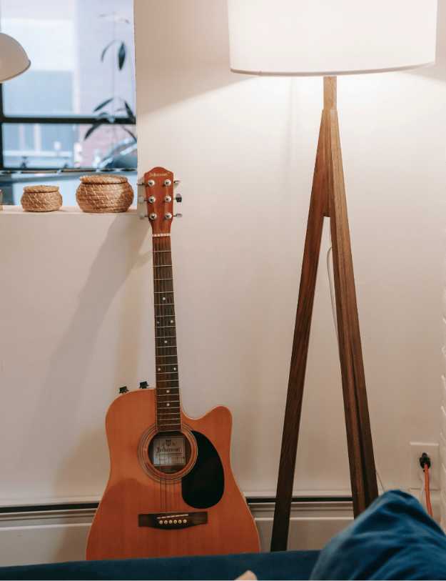 A guitar leaning against a wall next to a lamp.
