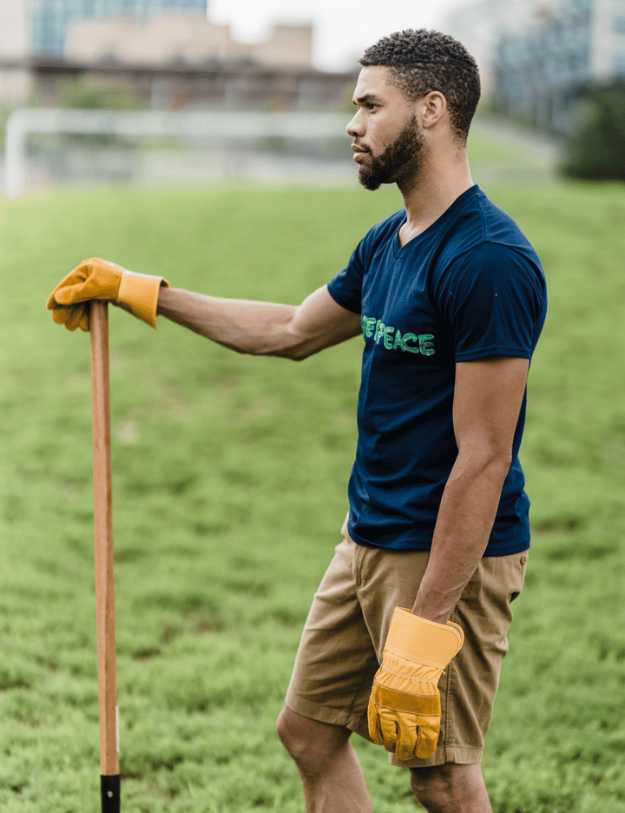 A colored man holding a shovel with gloves in a yard.