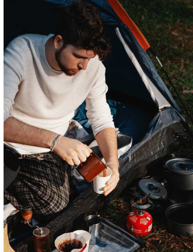 A man pouring a drink while sitting up in a tent.