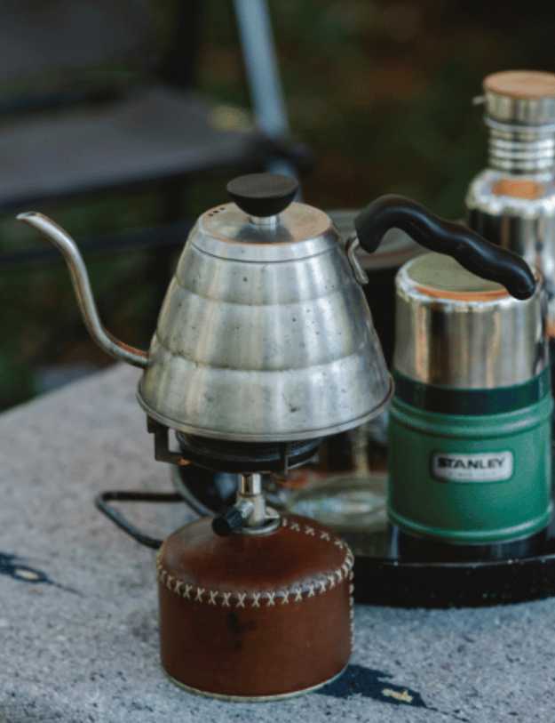 A kettle on a burner next to camping kitchen utensils. 
