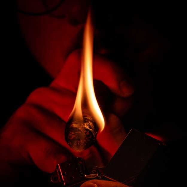 A man in the dark lighting a cigar with a zippo lighter