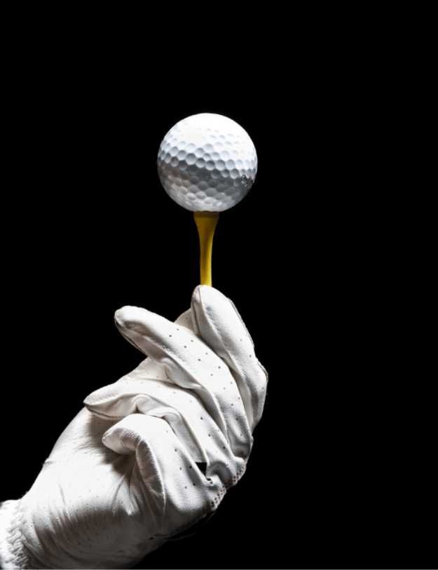Person with gloves on holding a tee with a golf ball on it