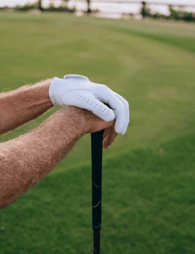 Man in a golf course holding his club with both arms