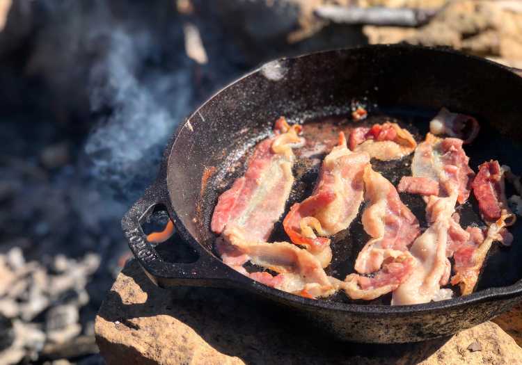 Grilling bacon over coals in a cast iron pan!