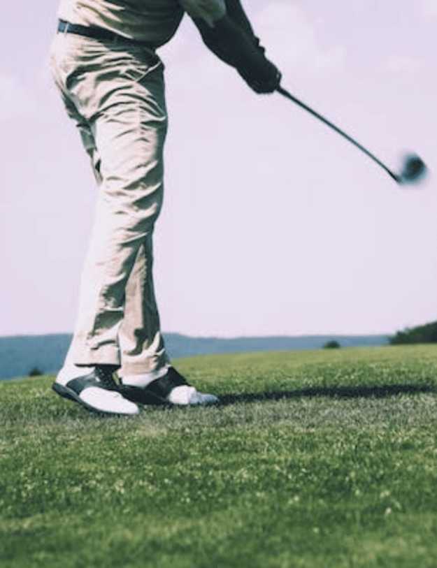 A close up of a mans shoes as he is mid-swing