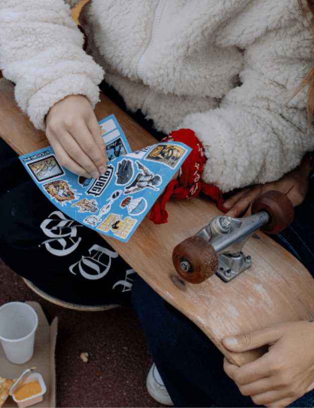 Two people sitting down putting stickers on a skateboard