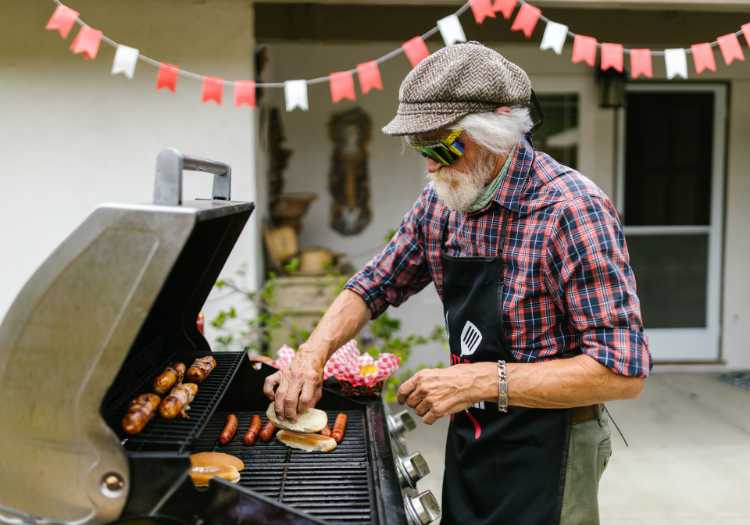 Older man grilling hotdogs and hamburgers at a party!