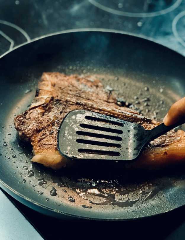 A Crispy piece of steak being pressed on with a spatula