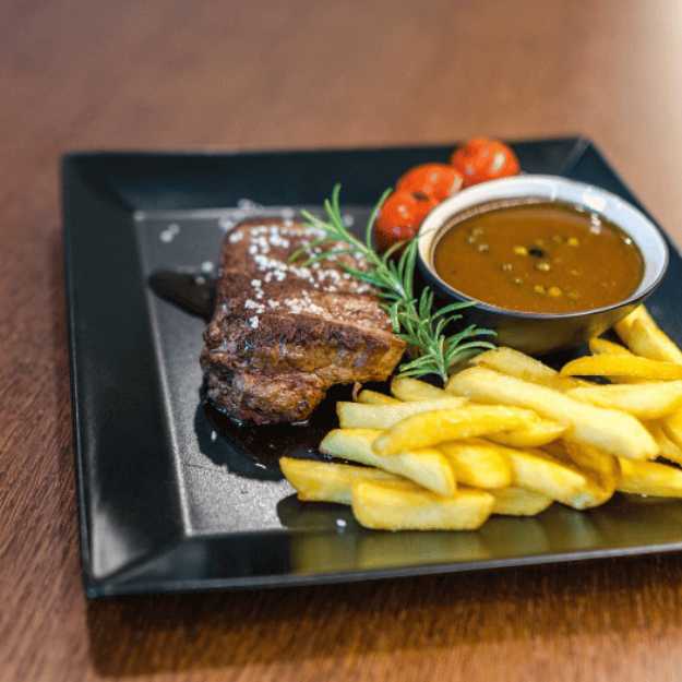 A Restaurant display of steak and fries paired with a sauce in a bowl.