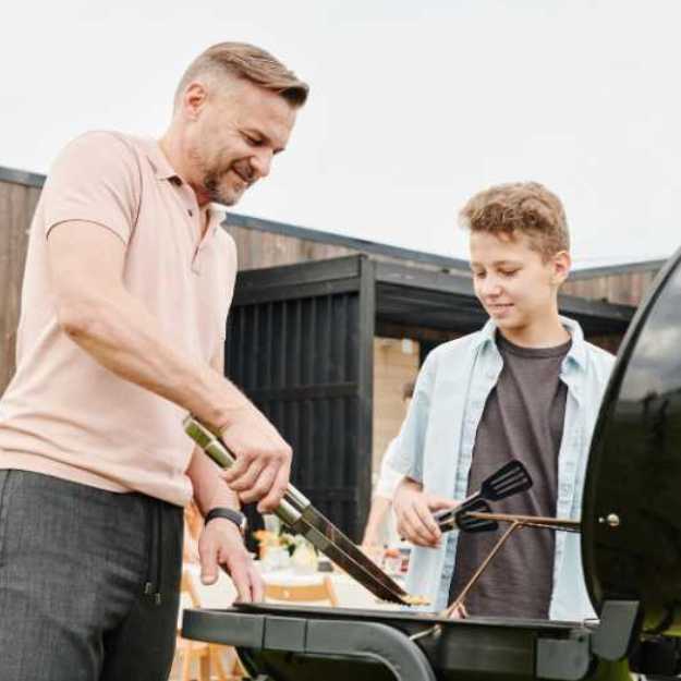 A Man and a boy both grilling outisde.