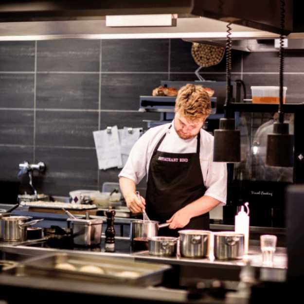A Chef whisking a bowl in a restaurant kitchen.