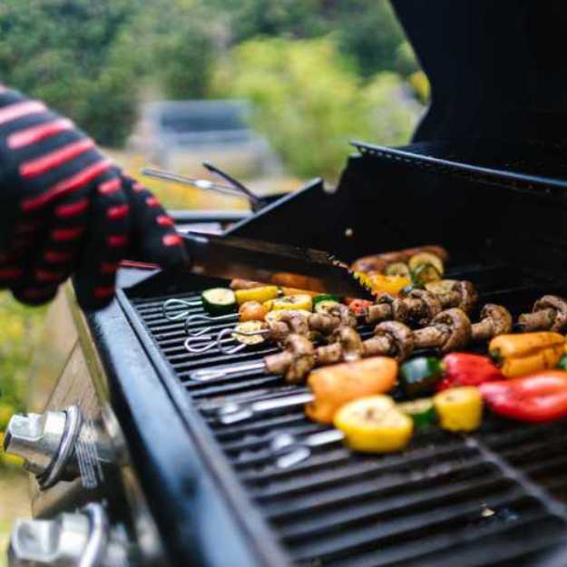Side view of someone flipping kebabs around on a grill.
