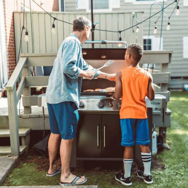 A White man and colored child at a grill outisde.