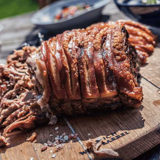 Meat wrapped with bacon being pulled apart on a cutting board outside.
