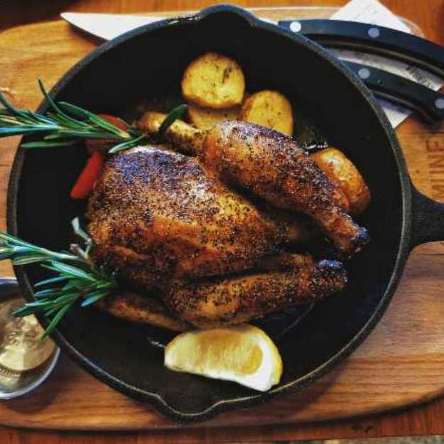 A Whole chicken in an iron pan with lemons and herbs.