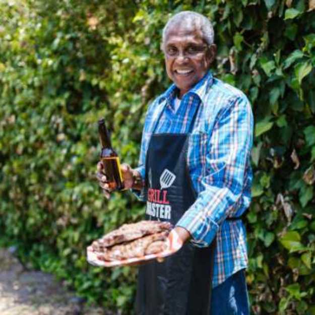 A Colored man holding a plate of meat with one hand and a beer with the other.