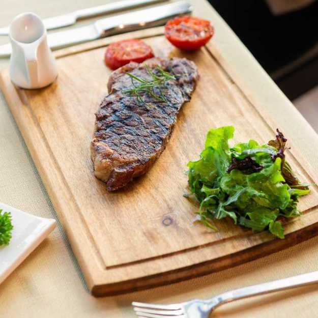 A Grilled steak on a cutting board with veggies and utensils.