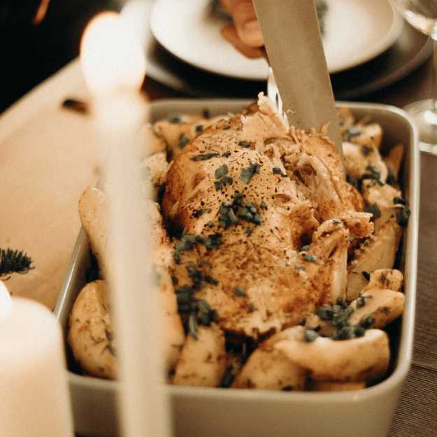 A Thanksgiving turkey in a bowl with herbs on a table with candles.