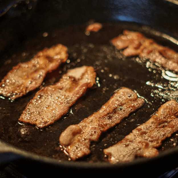 Bacon being cooked on a pan.