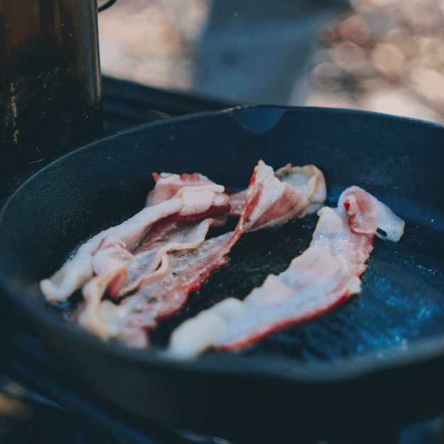 Turkey bacon being cooked on ironcast pan.
