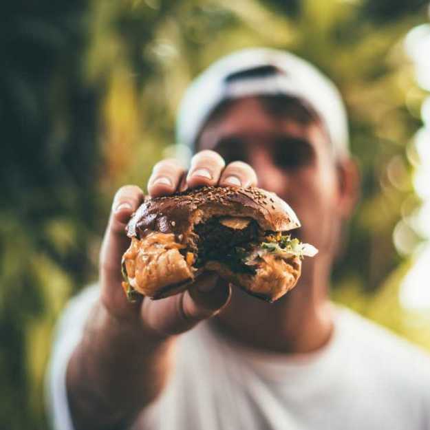 A man holding out a bitten into burger.