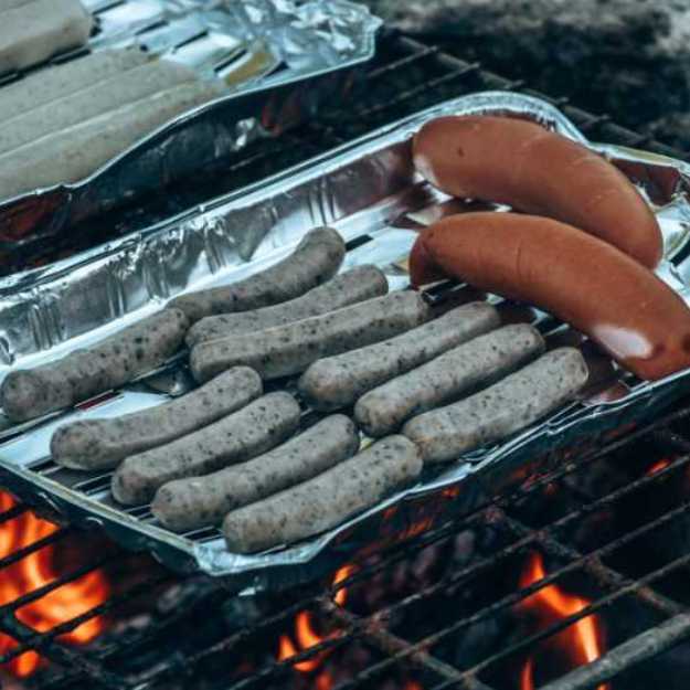 Wieners and buns on a foil tray on an outdoor grill.