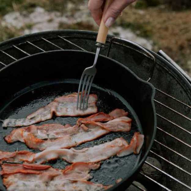 Someone poking bacon in an iron pan.