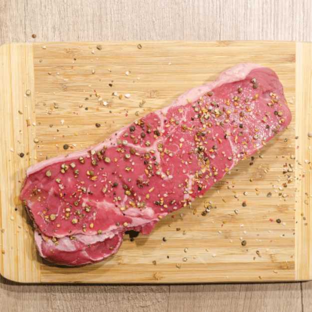 A Steak on a cutting board with seasoning on it.