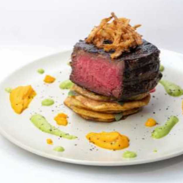 A Rare filet mignon on onion rings decorated with sauces.