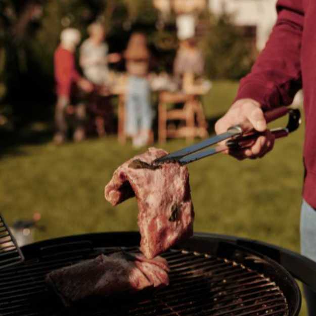 Person holding a steak over a grill with tongs.