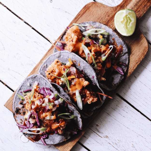 Purple tortilla tacos on a hand held cutting board.
