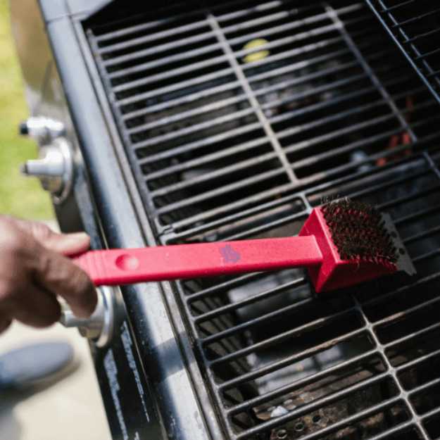 Someone cleaning a grill with a brush.