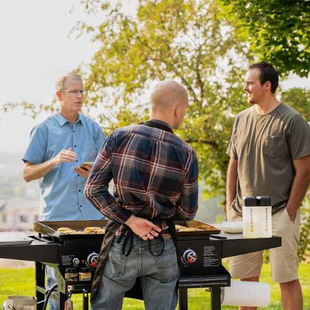 Three men cooking outside with a griddle.