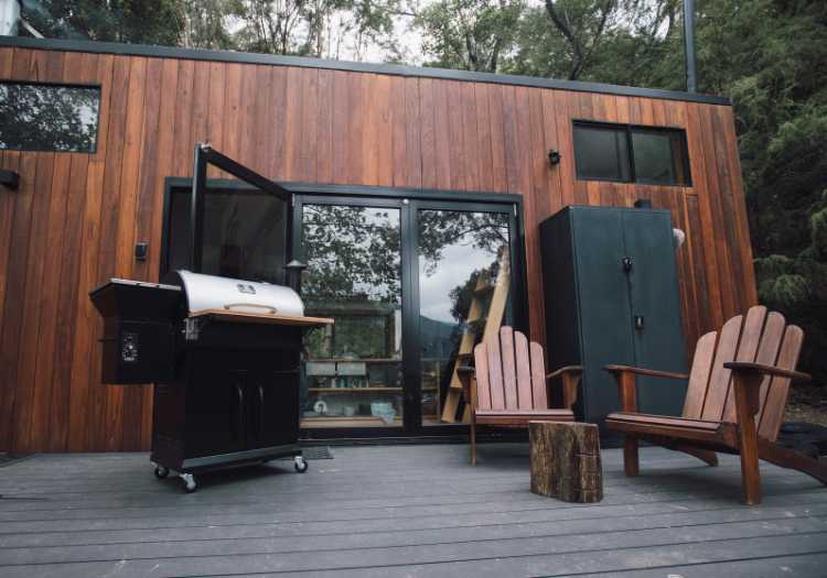 A pellet grill on a back porch with chairs
