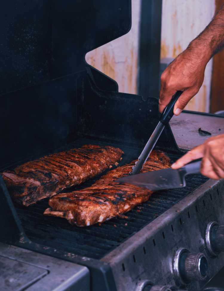 Man cutting open a prime rib while being grilled. 