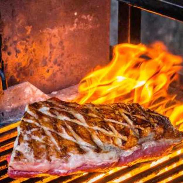 A Steak being grilled with high flames.