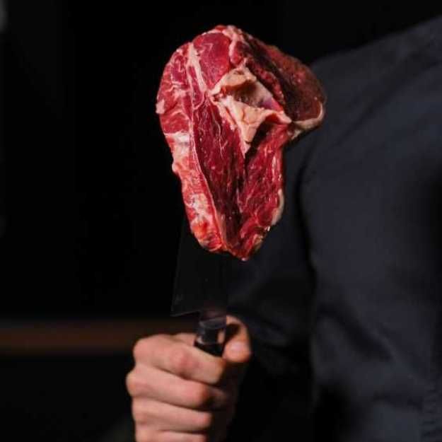 Someone holding a raw steak with a knife.