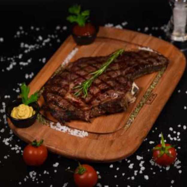 A Steak on a cutting board with veggies and salt scattered around it.