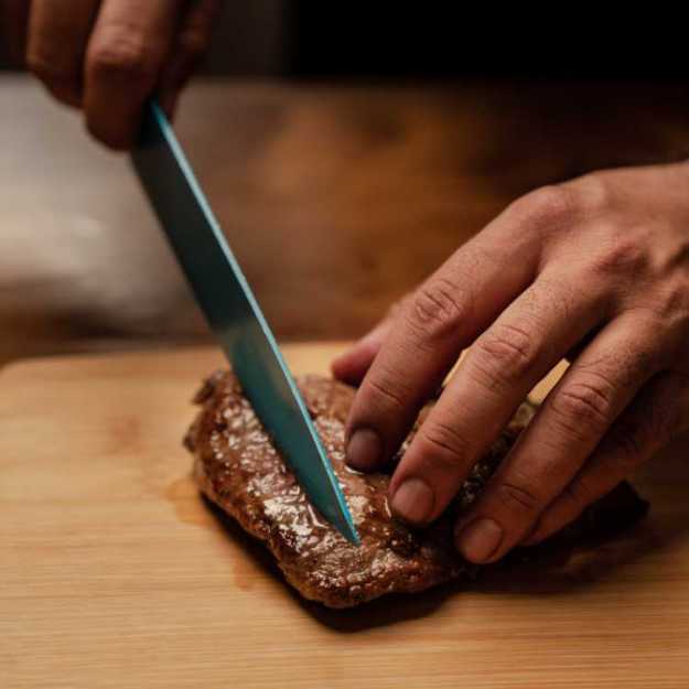 Someone holding a knife to a steak on a cutting board.