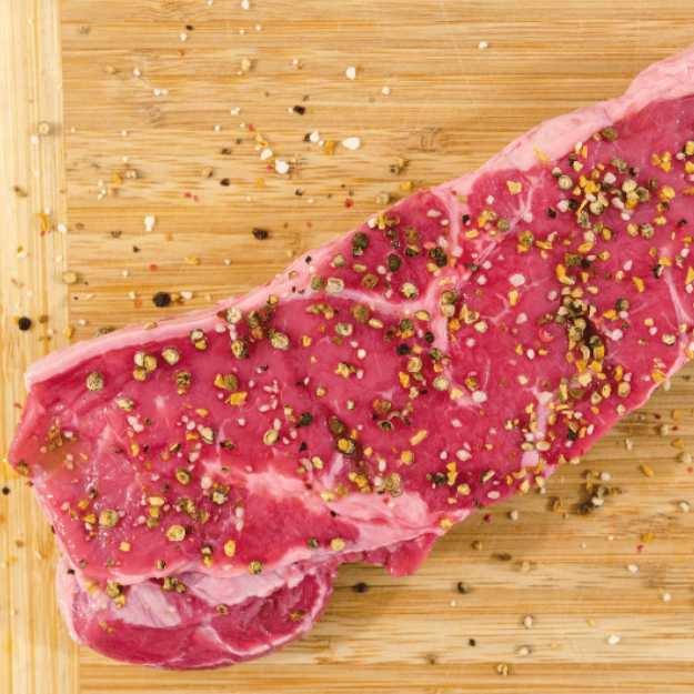 Uncooked steak on a chopping bored with seasoning.