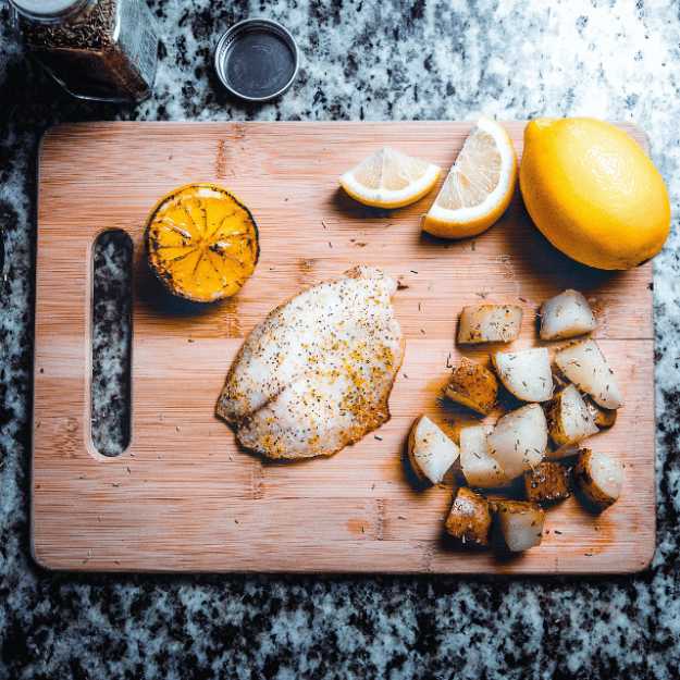 Fillet fish with chopped potatoes and lemons on a cutting board.