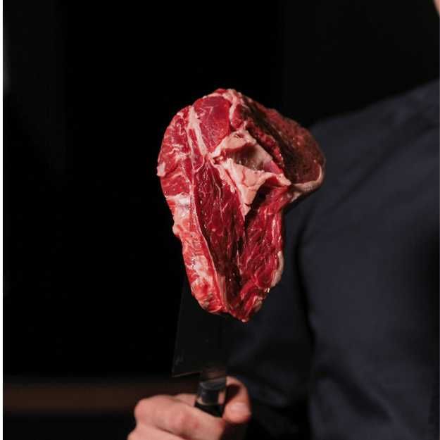 Someone holding a steak with a knife.