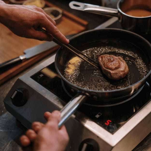 A small steak in a pan being seared and buttered.