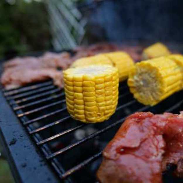 Corn and raw meat cooking on a grill.